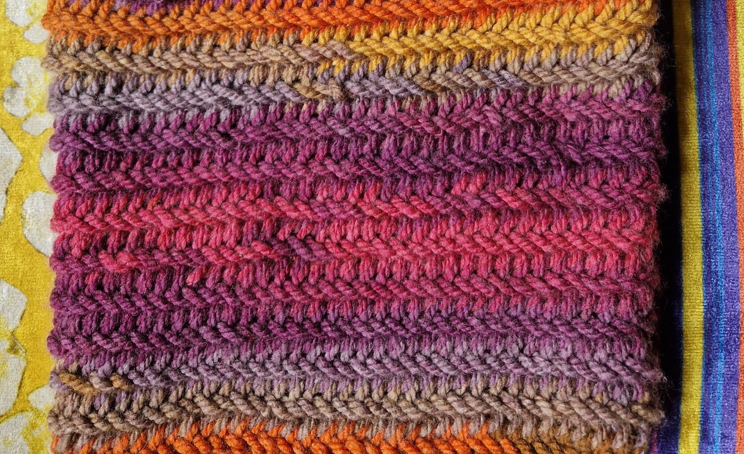 A picture of a tote bag made from yarn, in a rainbow of colours from oranges through to purples and pinks, and back again.